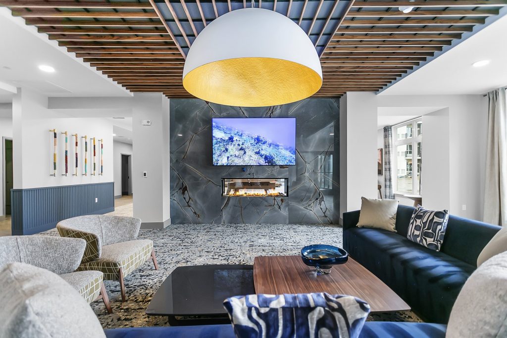 Modern lounge at Triton Square with slatted ceiling, oversized gold pendant light, stone fireplace wall, and navy sofas.